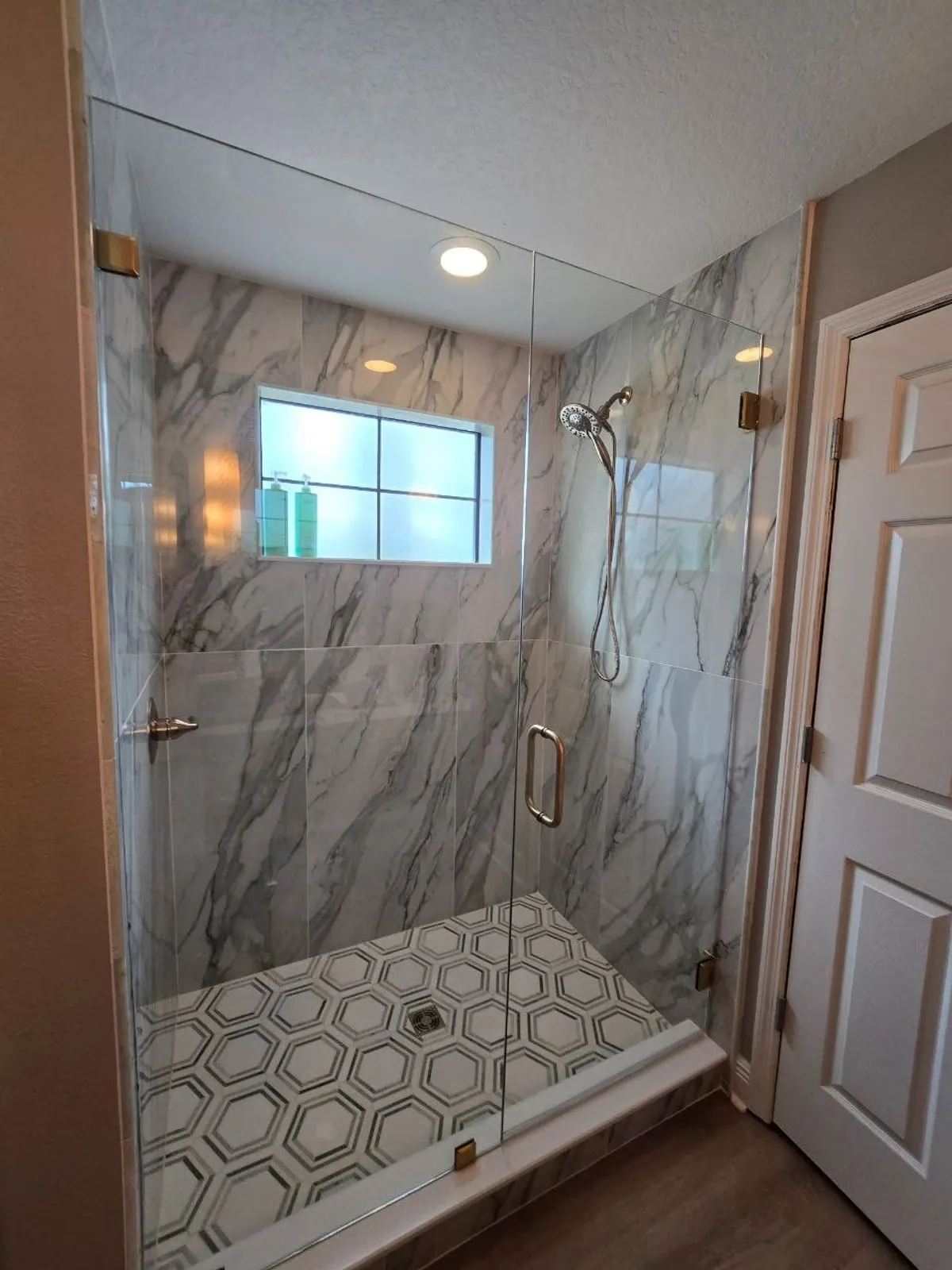 Marble walk-in shower with frameless glass, hex mosaic floor and brushed-gold fixtures