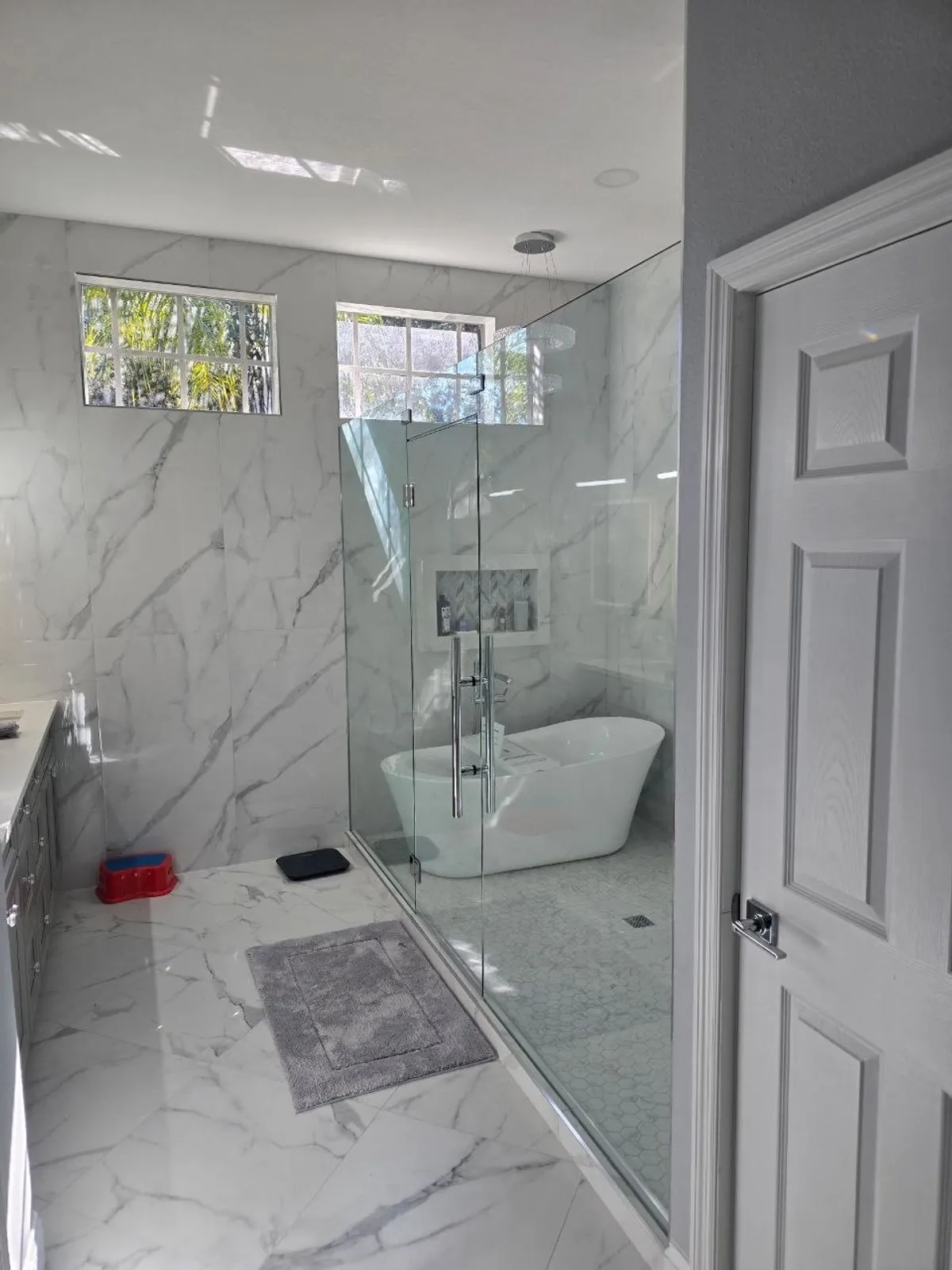 Freestanding soaking tub inside marble wet-room with frameless glass divider