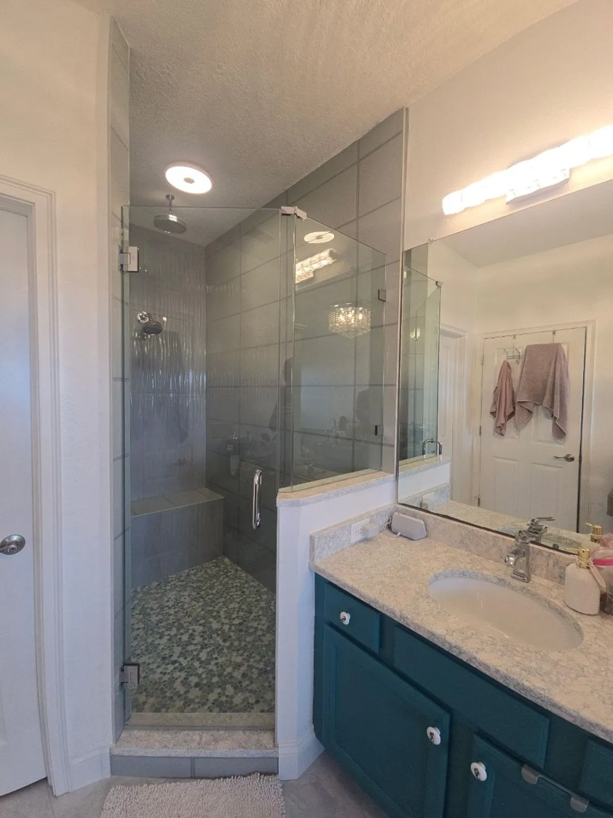 Corner glass shower with pebble floor, paired with deep-teal vanity and stone counter