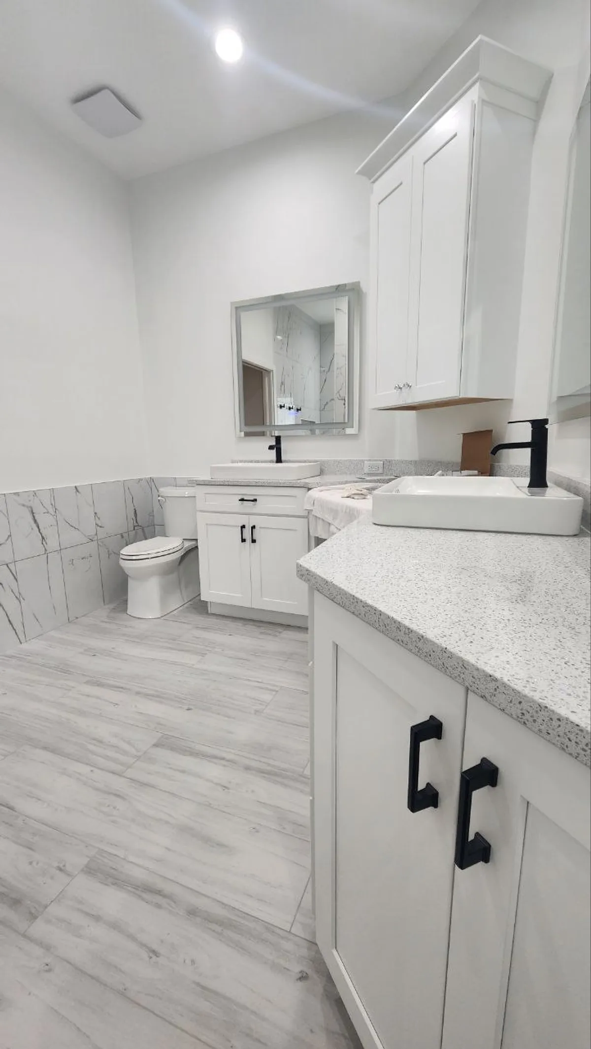 Modern powder bath with double vessel sinks, matte-black hardware and marble wainscot