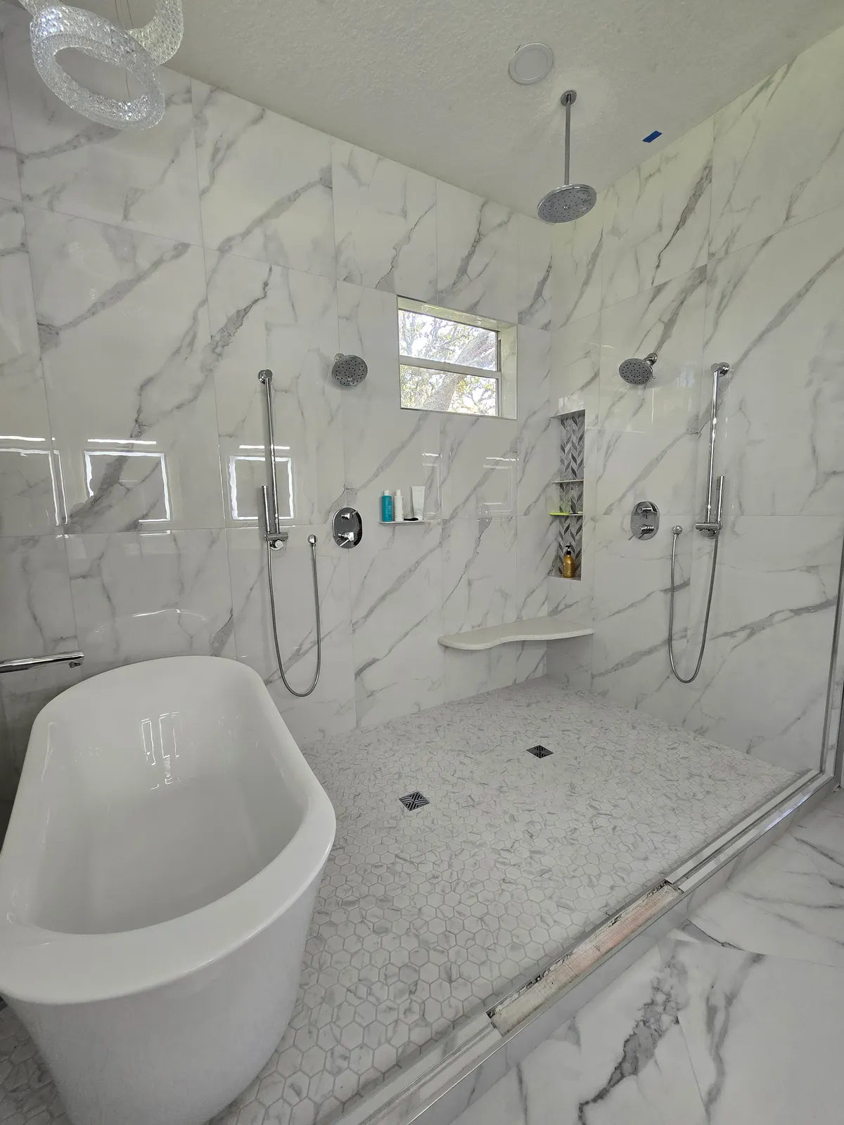 Walk-in marble shower with dual heads, niche and hex-mosaic floor